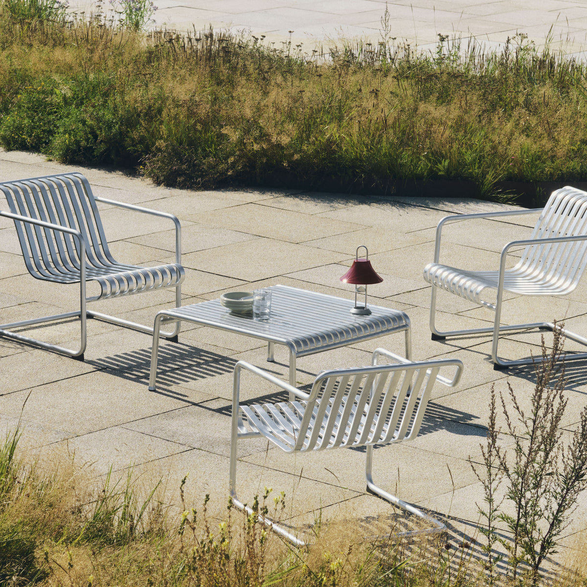 HAY Mousqueton Portable Lamp in iron red beside Palissade Cantilever lounge furniture outdoors