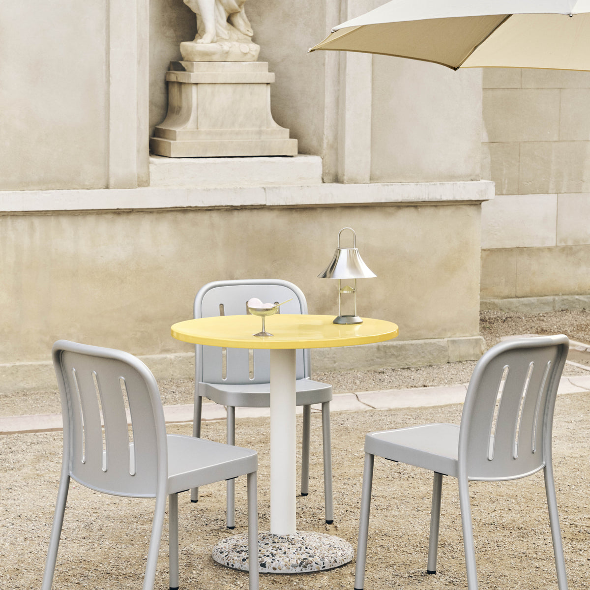 HAY Mousqueton Portable Lamp in stainless steel on a bright yellow Ceramic Table with Deville chairs